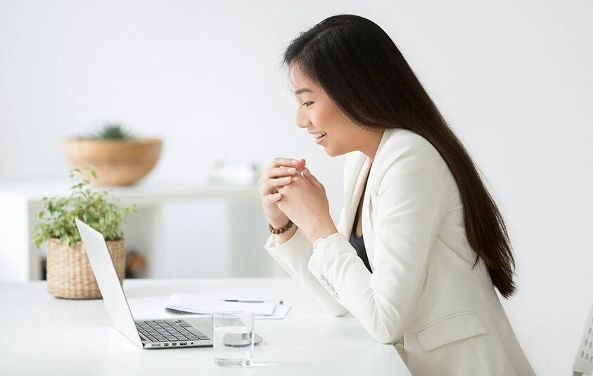 Smiling woman in a blazer engages with a laptop at a modern workspace